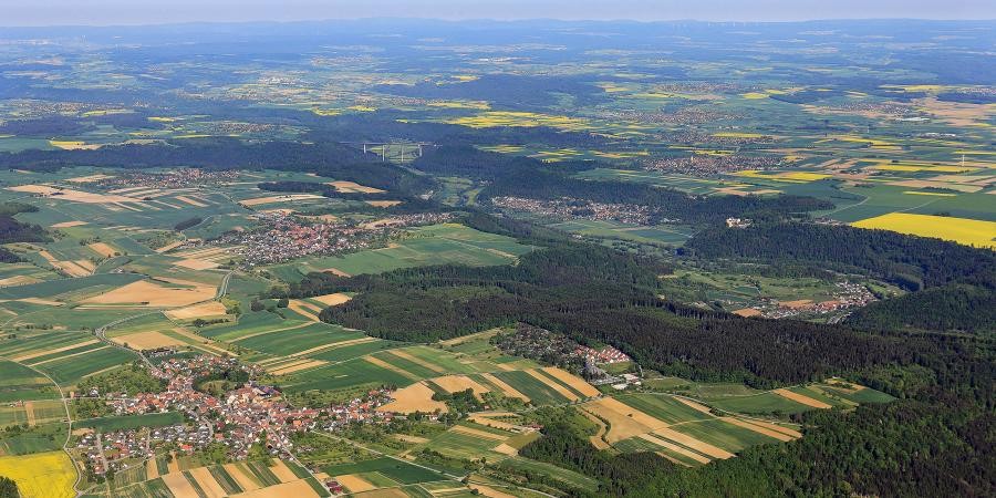 Aus der Luft gesehen mehrere Ortschaften, Felder und Waldgebiete, im Hintergrund die Schwarzwaldberge