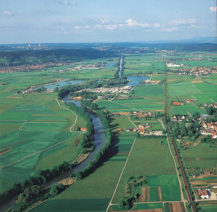 Luftbild, der Fluss Neckar, bestanden mit Bäumen, verläuft vom Vordergrund in den Hintergrund, umgeben von Feldern und Ortschaften, im Mittelgrund beidseits Baggerseen, im Hintergrund Berge
