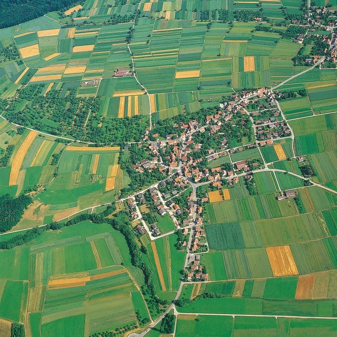 Luftbild einer Ortschaft, umgeben von in schmale Streifen aufgeteilten Feldern