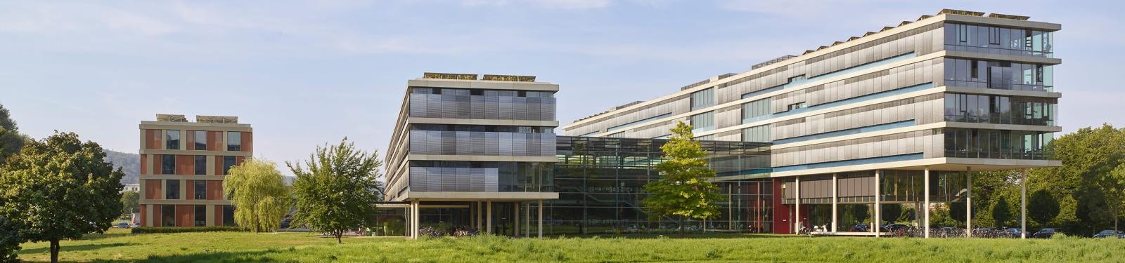 Drei lange, mehrstöckige, annähernd parallel angeordnete und teils querverbundene Gebäude, umgeben von Wiesen mit Bäumen.