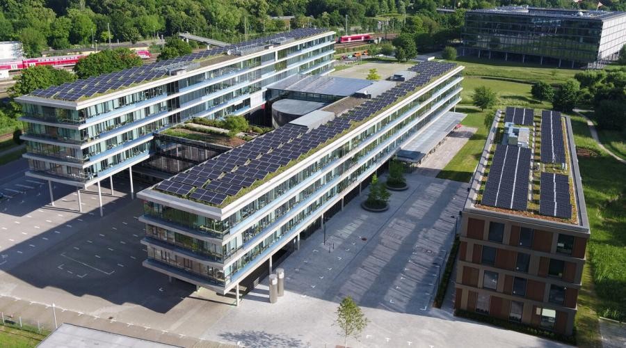 Landratsamt Tübingen Drei vier- bis fünfstöckige Gebäuderiegel, in etwa parallel angeordnet, die beiden langen Riegel stehen auf Stelzen und haben zwei verbindende Gebäudeteile, auf den Dächern sind Fotovoltaikanlagen, in der Umgebung Wiesen und Bäume