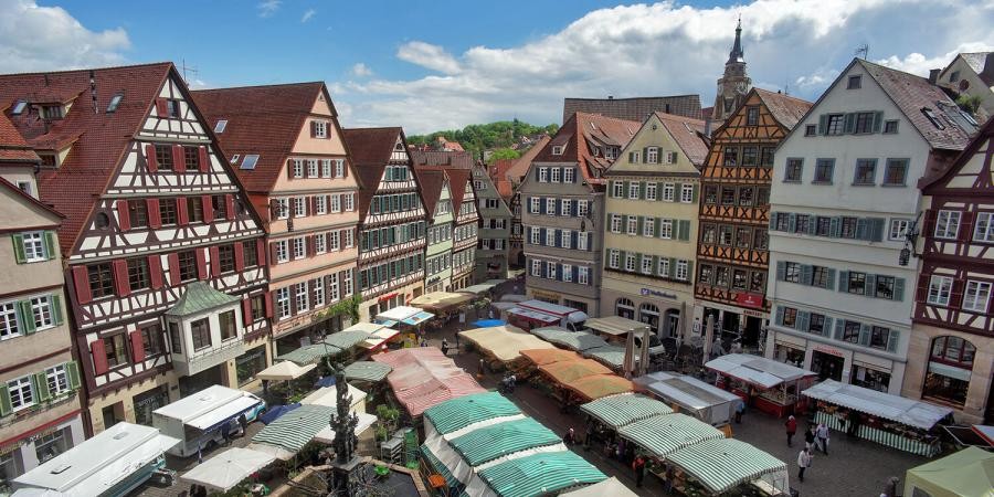 Marktplatz Tübingen Marktplatz, umstanden von großen historischen Häusern, giebelständig und aneinandergebaut, teils mit Fachwerk, von oben gesehen mit Marktständen, dazwischen ein Brunnen