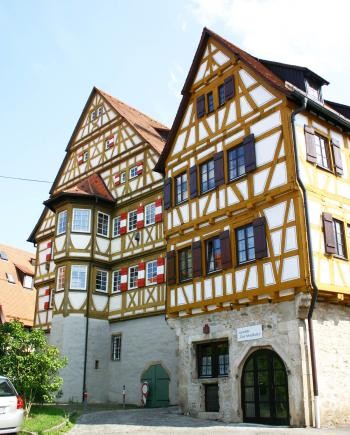 Giebelansicht von zwei nebeneinander angeordneten Fachwerkgebäuden auf Steinsockeln, am linken Gebäudeteil ein vorgesetzter Erkeranbau