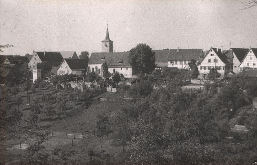 Historische Fotografie, Ortsansicht Wolfenhausen, mit Häusern am Ortsrand und Kirchturm, davor Gärten und Baumwiesen in leichter Hanglage