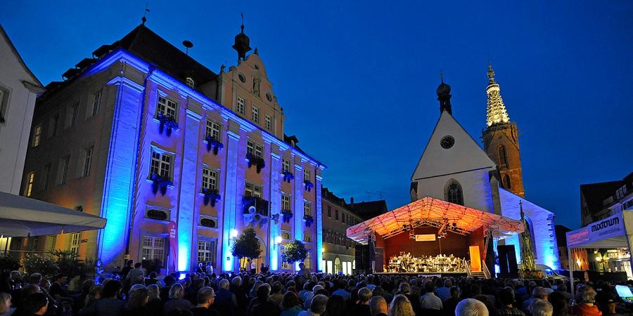 Beleuchtete Open-Air-Bühne, auf dem Platz sitzen viele Menschen in Stuhlreihen, zu sehen ist das barocke Gebäude des Rathauses und die Domkirche mit spätgotischem beleuchtetem Turmhelm
