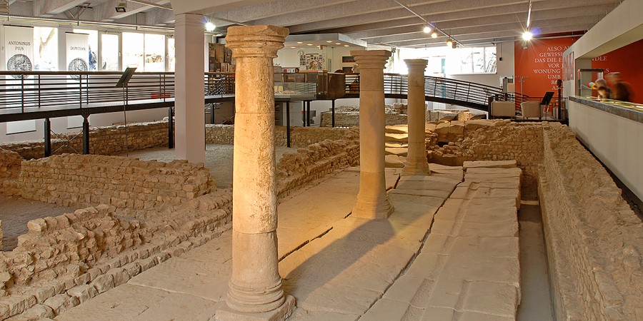 Innenraum mit römischen Säulen und einem Graben, Mauerresten und Wandmalereien, Metallbrücken für die Besichtigung