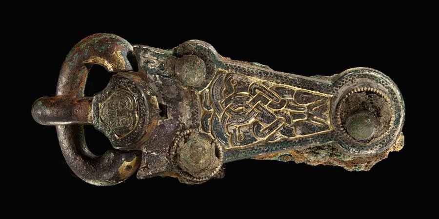 Schnalle aus Metall, mit ornamentaler Verzierung, am Ansatz des Dorns ein Gesicht