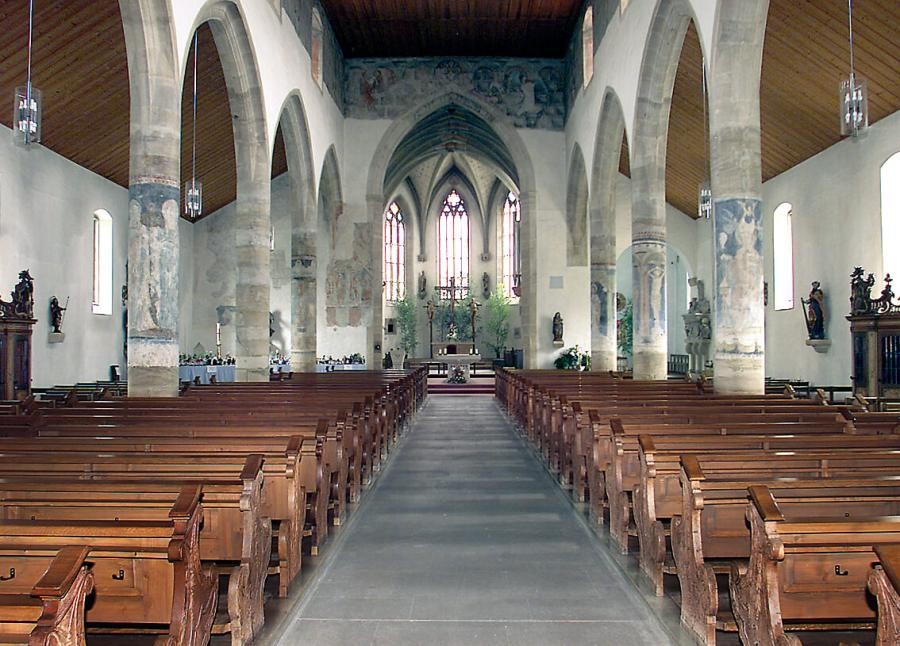 Innenraum einer Kirche als Basilika in gotischen Formen und flachgedecktem Hauptschiff und Seitenschiffen, an den Rundsäulen zwischen Haupt- und Seitenschiffen und über dem Triumphbogen vor dem Chorraum  sind Wandmalereien zu sehen
