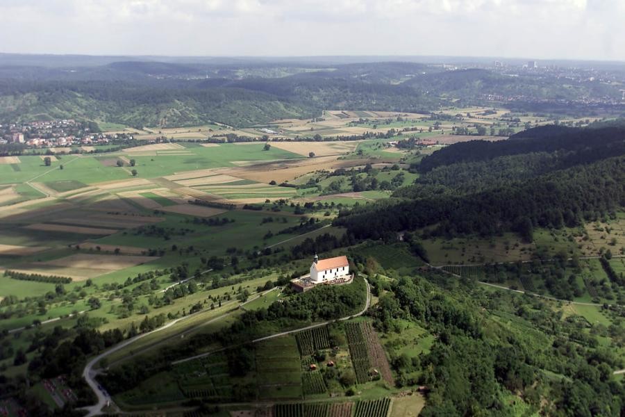 Bergrücken mit Wurmlinger Kapelle, im Hintergrund ein Tal mit Ortschaften und bewaldete Landschaft