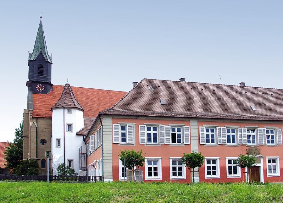 Schlossgebäude, zweistöckig mit Walmdach, dahinter eine Kirche mit Dachreiter, dazwischen ein mehreckiger Turm