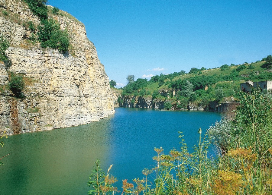 Felswand, davor ein Gewässer, auf der anderen Seite bewachsene Landschaft
