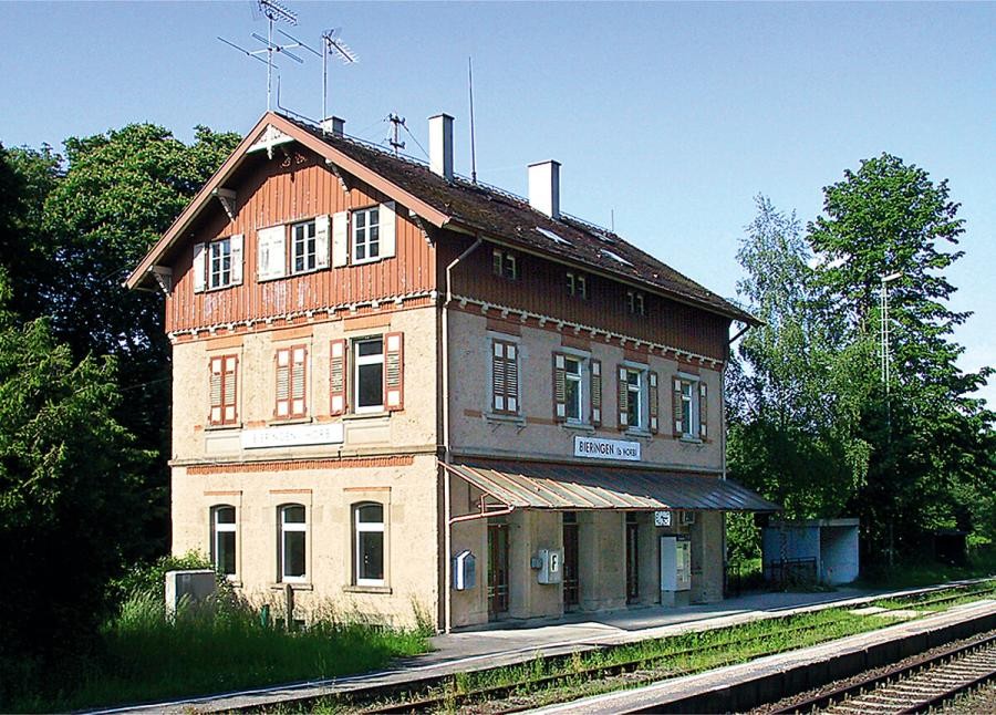 Bahnhofsgebäude an Bahngleisen, dreistöckig mit Satteldach, das Dachgeschoss mit Holz verkleidet, am Bahnsteig entlang der Längsseite des Gebäudes eine Überdachung, darüber ein Bahnhofsschild "Bieringen" 