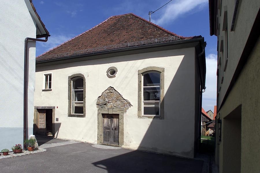 Gedenkstätte Synagoge Baisingen Außenansicht Gedenkstätte Synagoge Baisingen, kleineres walmdachgedecktes Gebäude steht in dichter umgebender Bebauung, außen sind Spuren der Verwüstung wie fehlender Putz über der Tür erkennbar