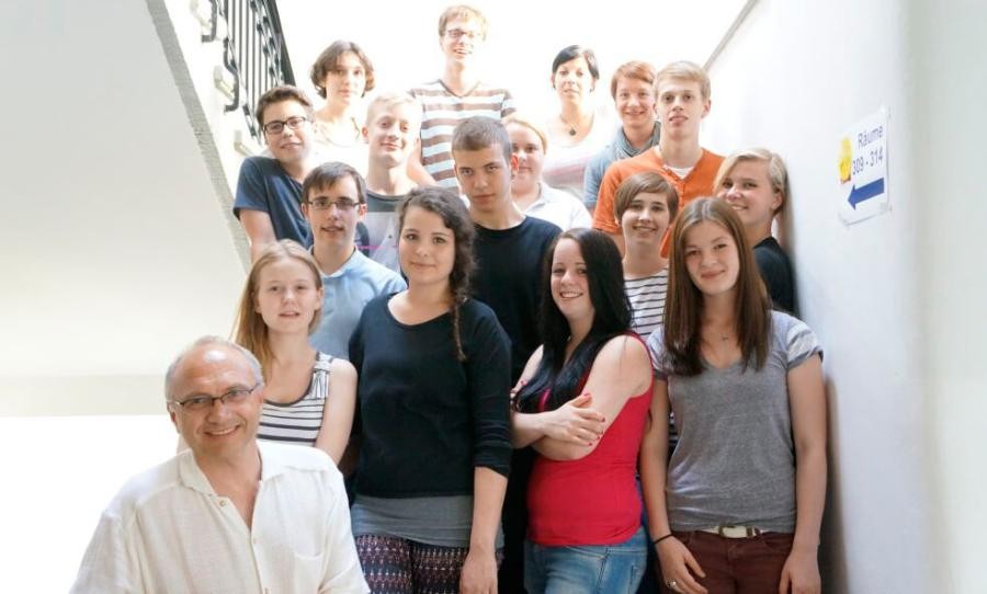 Eine Gruppe von jungen Personen und einer älteren Person steht auf einer Treppe in einem Gebäude