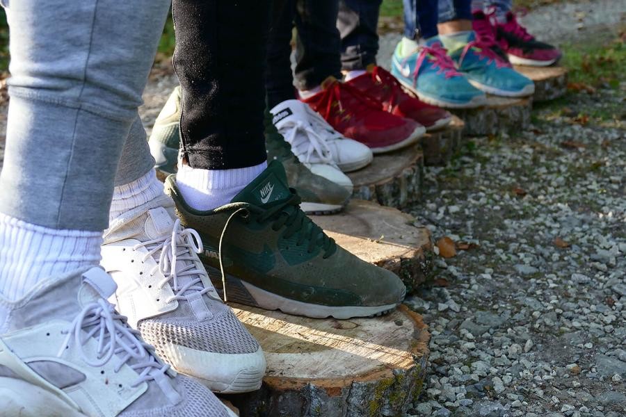Kinder stehen auf einem Weg aus Holzscheiben, zu sehen sind eine Reihe von Füßen mit Turnschuhen