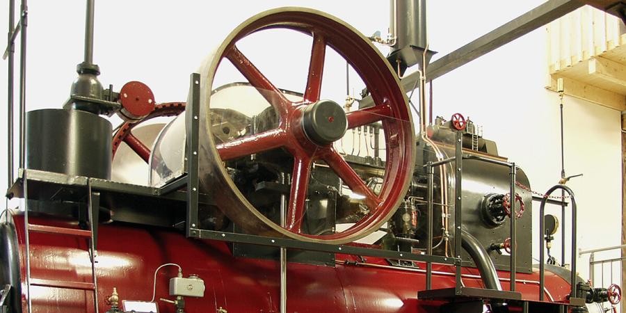 Teil einer Dampfmaschine mit, Dampfkessel, großem Schwungrad und mechanischen Teilen