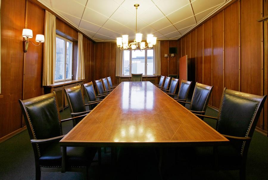 Raum mit Holztäfelung, länglicher Tisch mit beidseits Stühlen, zwei Fenster