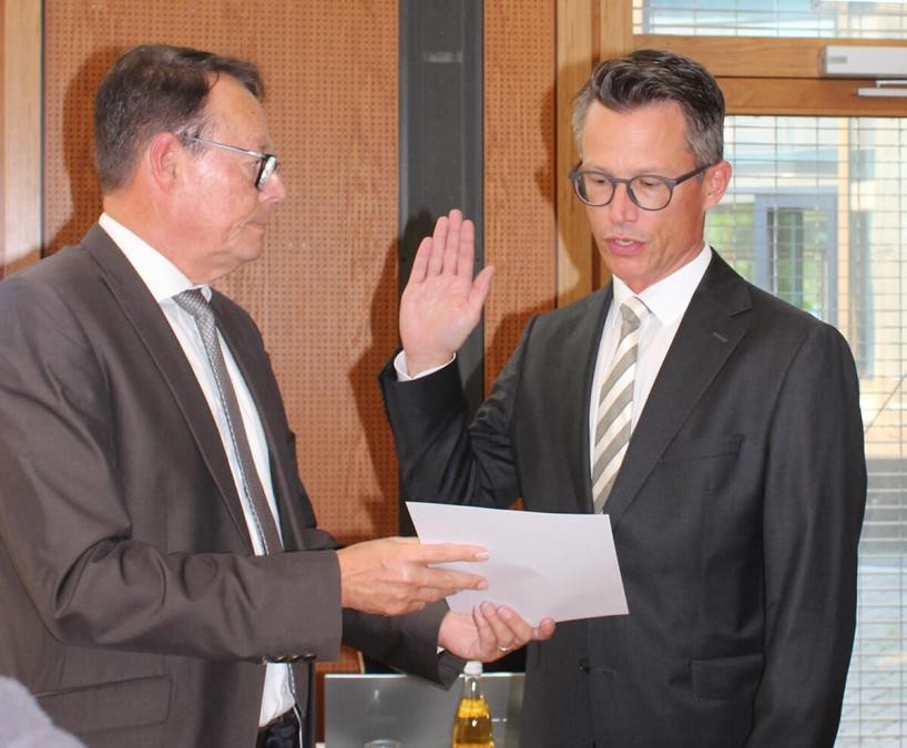 Regierungspräsident Klaus Tappeser hält ein Dokument und Landrat Dr. Hendrik Bednarz hebt die Hand zum Amtseid