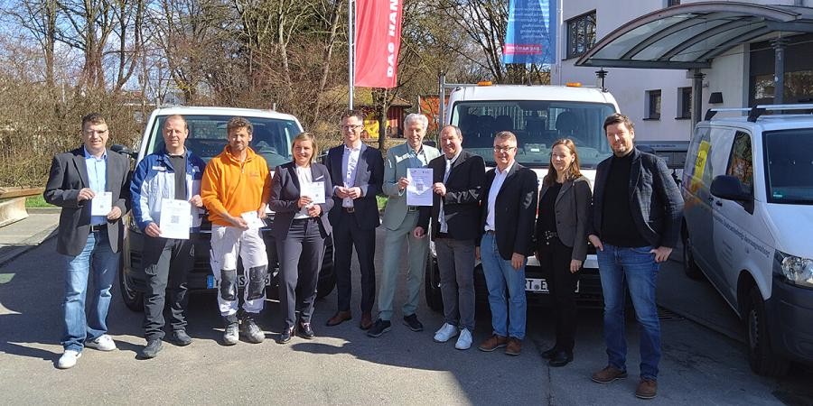 Gruppe von Personen, einige halten den Handwerkerparkausweis in der Hand, im Hintergrund Fahrzeuge von Handwerksbetrieben