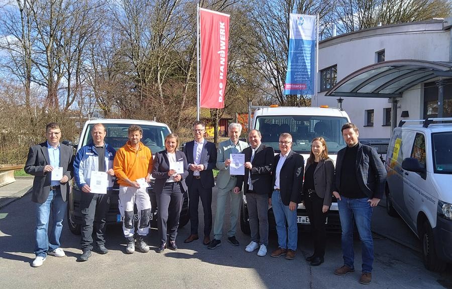 Gruppe von Personen, einige halten den Handwerkerparkausweis in der Hand, im Hintergrund Fahrzeuge von Handwerksbetrieben