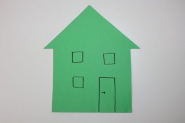 Ein Haus, ausgeschnitten aus Papier, darauf gezeichnet eine Tür und drei Fenster