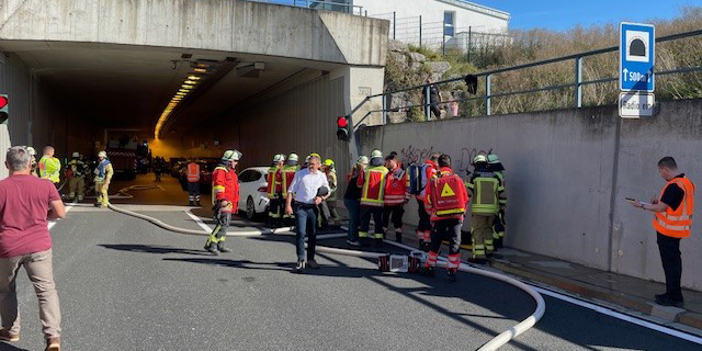 Tunneleingang, mehrer Personen in Rettungswesten arbeiten zusammen, im Tunnel sind Autos und Einsatzkräfte zu sehen.