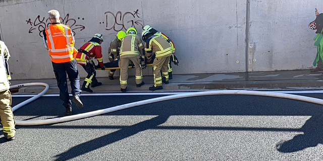 Mehrere Einsatzkräfte mit Schutzkleidung arbeiten an einer Betonwand zusammen, ein Schlauch liegt auf der Fahrbahn