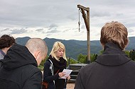 Gruppe von jungen Personen im KZ Natzweiler, Elsass, auf einem Berg bei einem Galgen, eine Frau liest einen Te