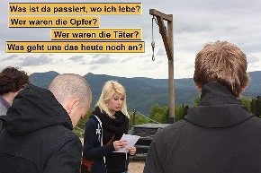 Mehrere Personen stehen auf einem Berg im KZ Natzweiler an einem Galgen, eine Frau liest einen Text. Beschriftung: "Was ist da passiert, wo ich lebe? Wer waren die Opfer? Wer waren die Täter? Was geht uns das heute noch an?"