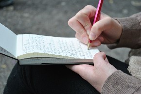 Eine Person hält einen Notizblock auf den Knien und schreibt