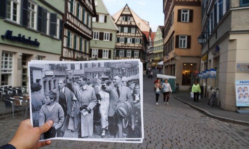 Ein Blick vom Marktplatz Tübingen Richtung Holzmarkt, eine Person hält ein altes Foto mit Personen die bei einer Versammlung an dieser Stelle den Hitlergruß zeigen 