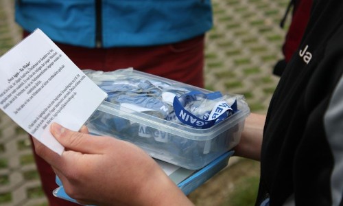 Eine Person hält eine Plastikdose mit Bändern und liest einen Text auf einem Zettel