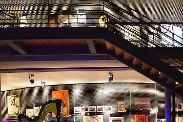 Mehrstöckicher Raum mit Fußgängerbrücke, Kunst-Ausstellung, eine Harfe ist teilweise zu sehen