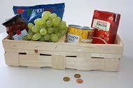 Spankorb mit Weintrauben und haltbaren Lebensmitteln, davor ein paar Münzen
