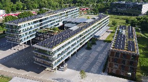 Luftbild des Landratsamts, es zeigt drei moderne Gebäuderiegel, vier- bis sechsstöckig, teils aufgestelzt, auf den Dächern Fotovoltaikpaneele, umgeben von Grün.