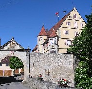 Torbogen und Mauer, dahinter ein mehrstöckiges historisches Schloss-Gebäude mit Türmchen und Erker.