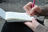 Eine Person schreibt auf einen Notizblock, zu sehen sind Hände Block und Bleistift